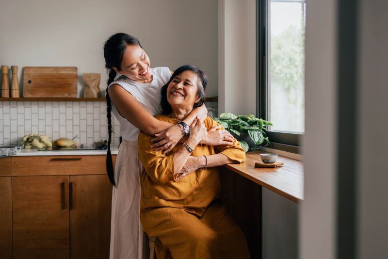 A photo of a granddaughter and grandmother hugging in a kitchen.