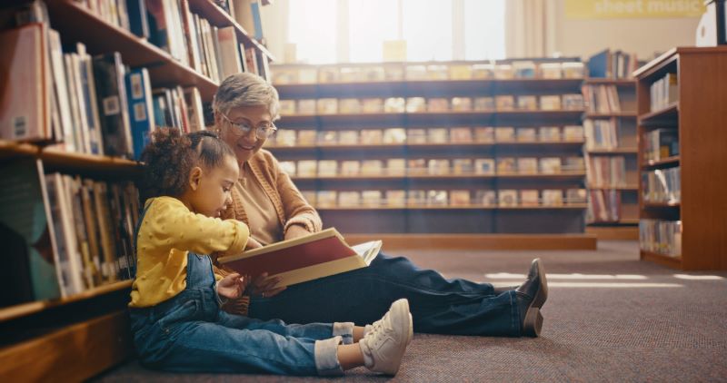A photo of a grandma and a granddaughter in a library. 